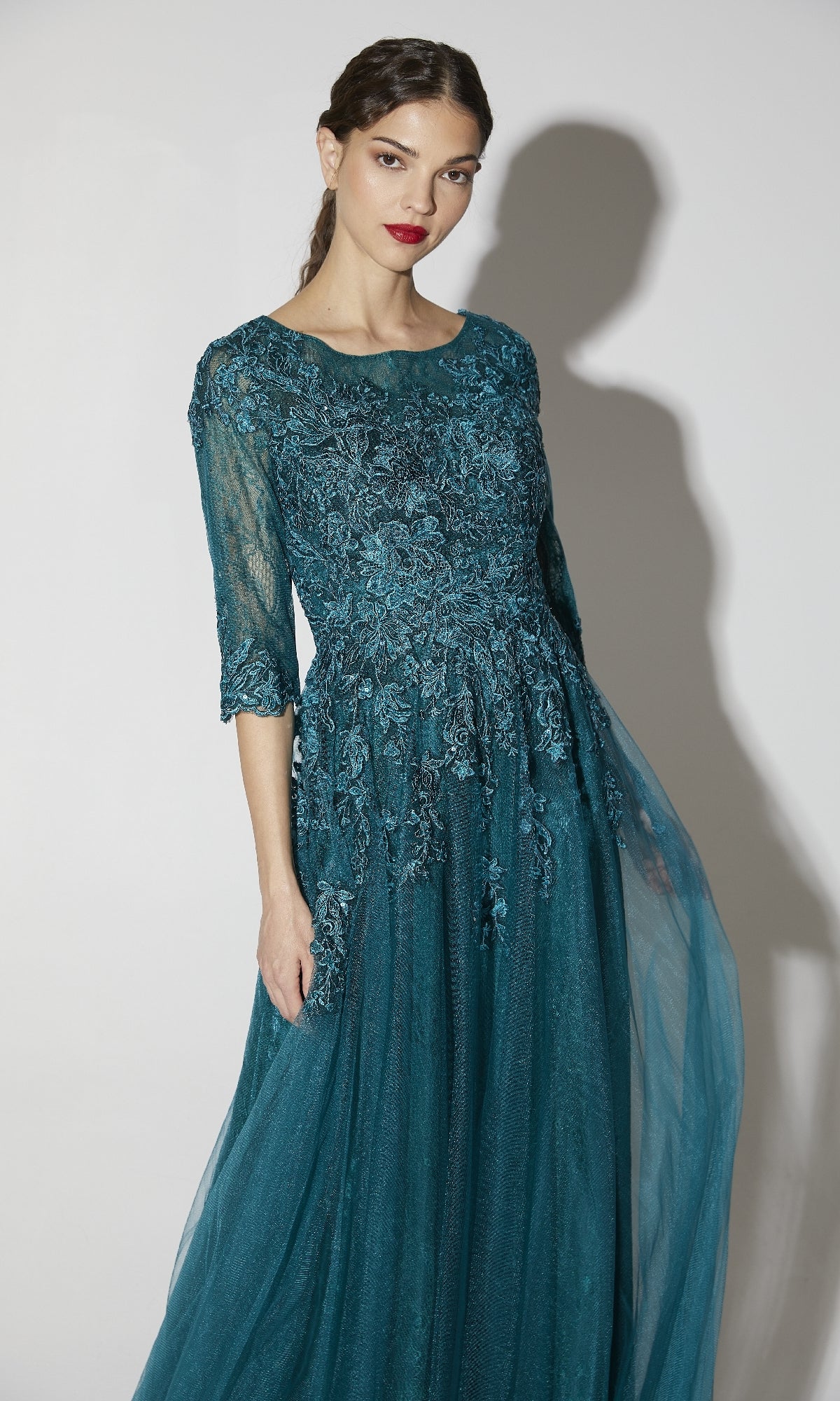 Woman wearing the Flowy Long Sleeve Long Formal Dress: Eureka 9660, featuring a teal lace bodice, tulle skirt, and three-quarter sleeves, standing against a plain light background.